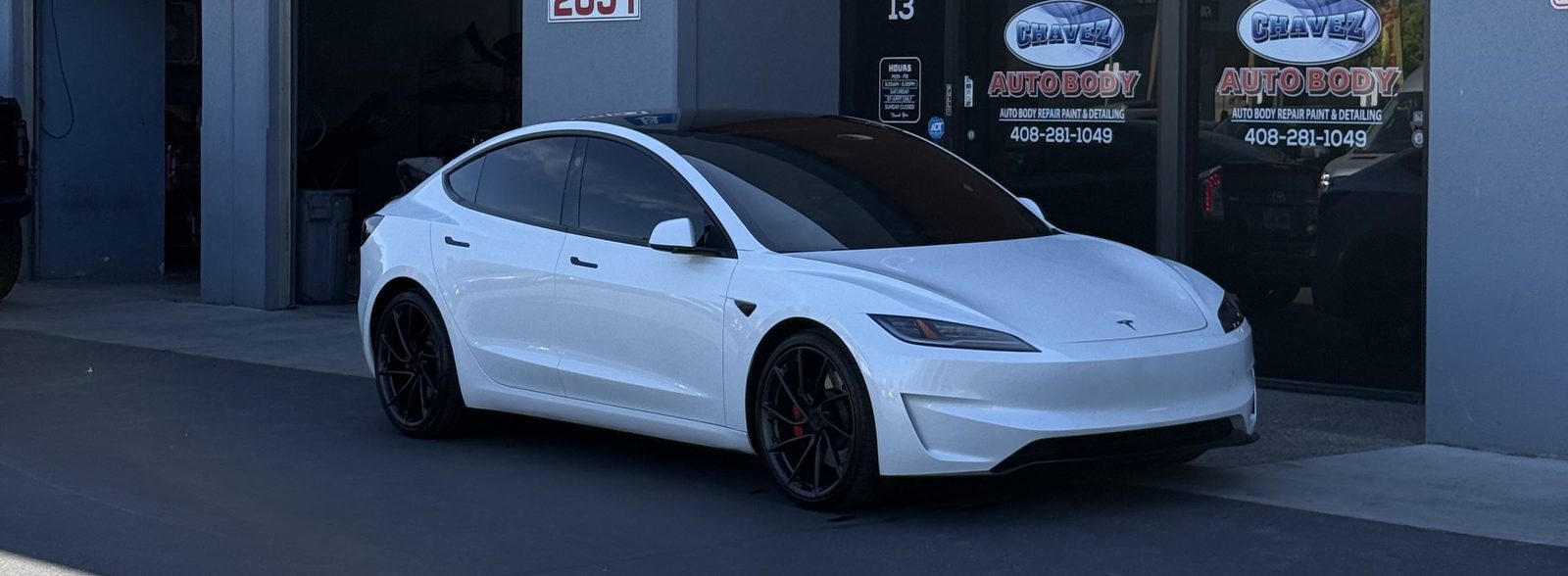 White Tesla Model 3 parked in front of the Chavez Auto Body shop doors on Monterey Road